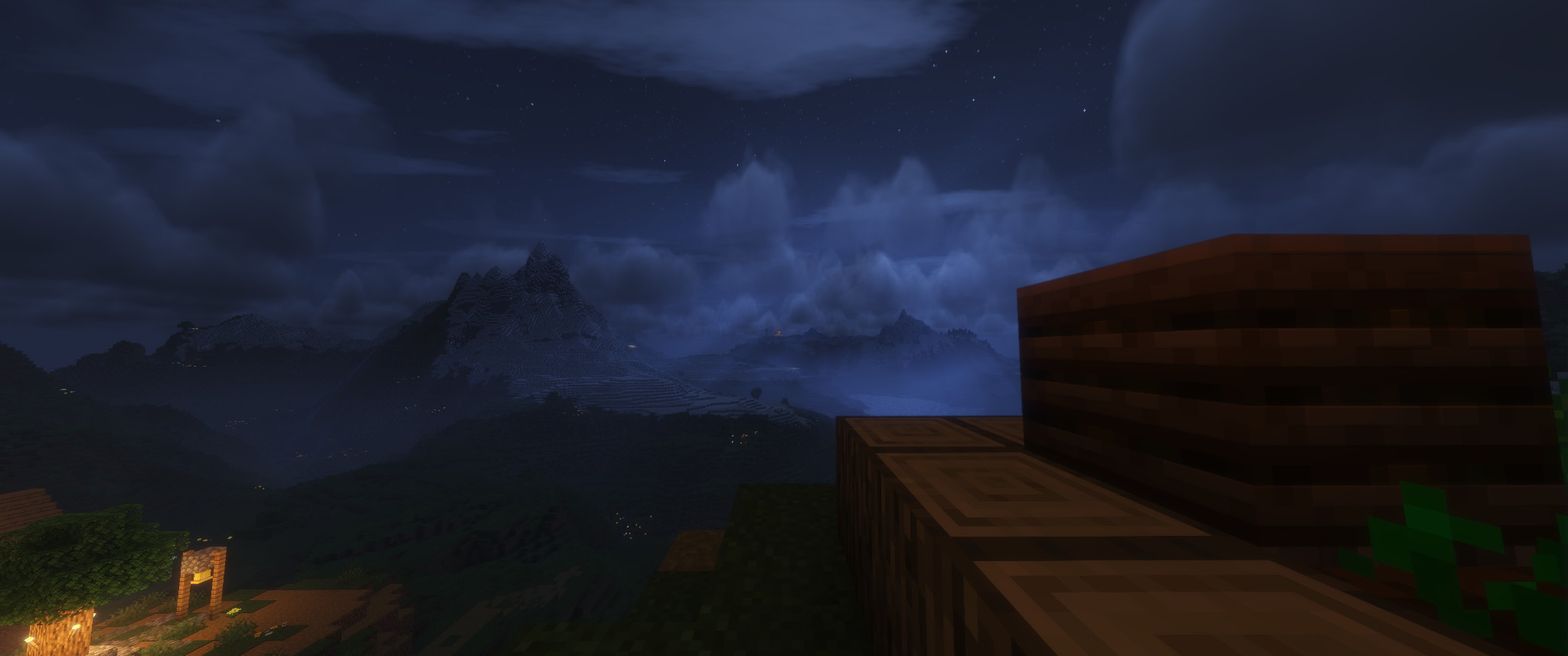 up close, logs from a farm, with farmland and a composting barrel. down to the left, the lights of a village. in the distance, a mountainous landscape, peaks piercing the clouds